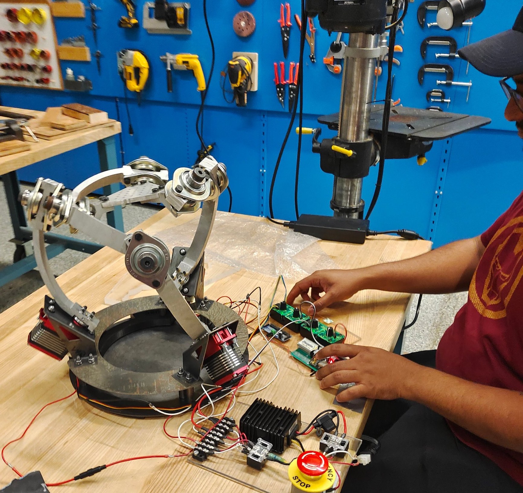 Ajay at a UBC Makerspace bench operating the rebuilt spherical parallel manipulator, with its servo controllers, power board and emergency stop in front of him