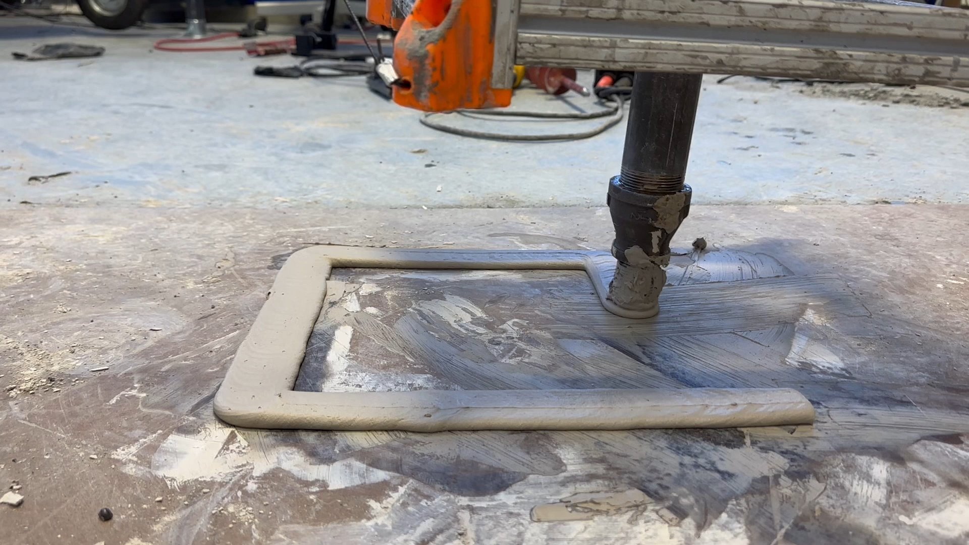 The printer's nozzle laying a continuous concrete bead on a site floor